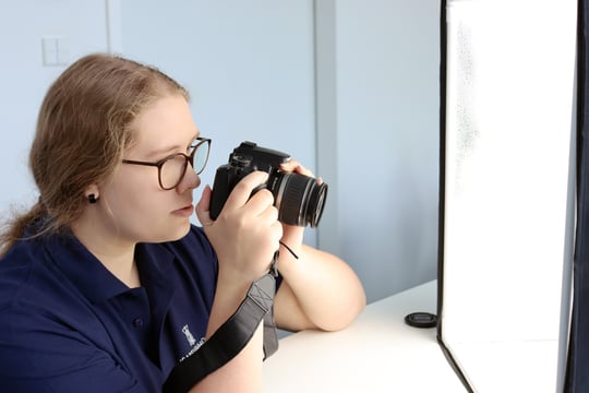 Auszubildende Mediengestalterin mit Kamera in der Hand schiesst Produktfotos