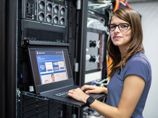 Jaqueline vor dem Laptop in die Kamera schauend