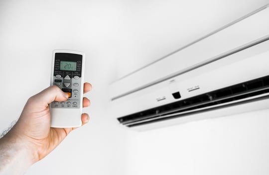 Hand holds the remote control in front of the air conditioner.